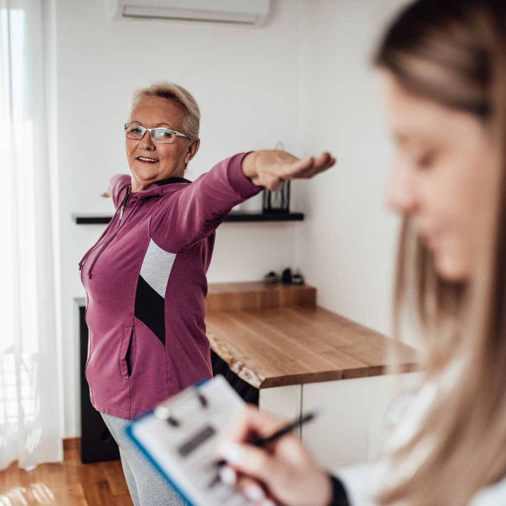 Eine junge Physiotherapeutin arbeitet bei einem Hausbesuch mit ihrer älteren Patientin zusammen.