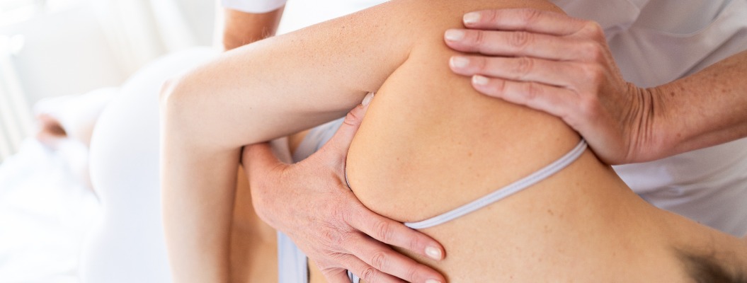 Eine Osteopathin führt bei einem Patienten eine Schulterblatttherapie durch