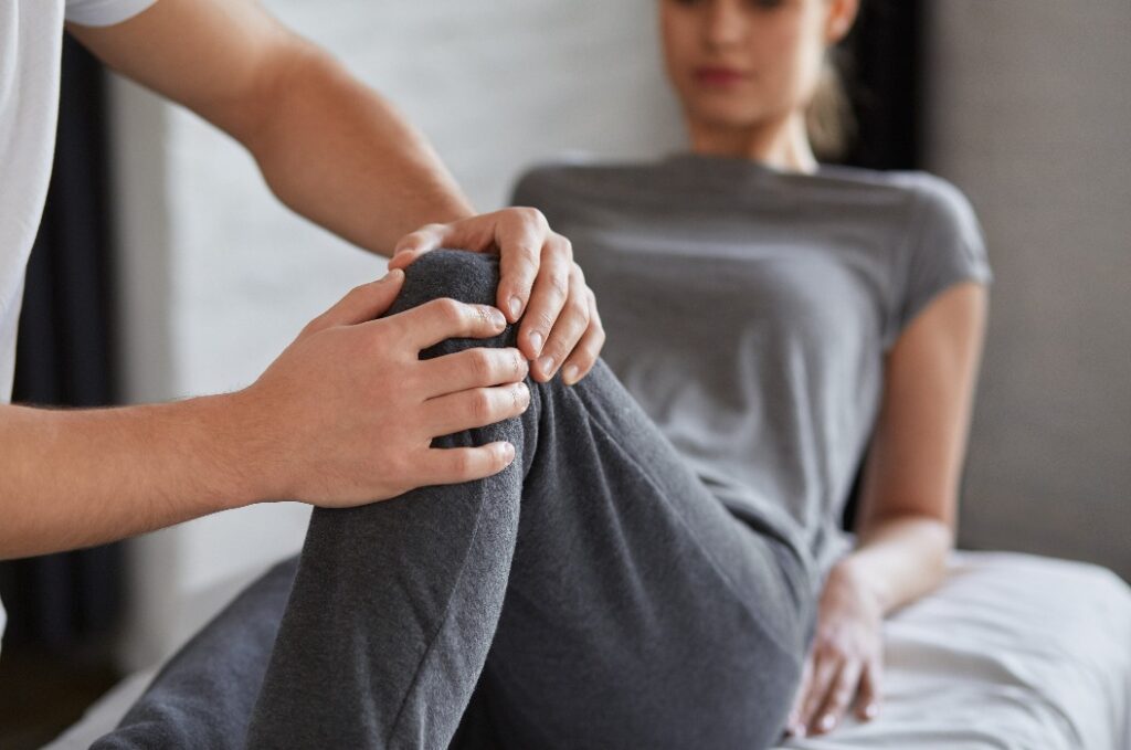 Eine Patientin führt gemeinsam mit einem Physiotherapeuten Übungen durch. Ein männlicher Therapeut behandelt das verletzte Knie eines jungen Sportlers. Posttraumatische Rehabilitation, Sportphysiotherapie, Rehabilitationskonzept
