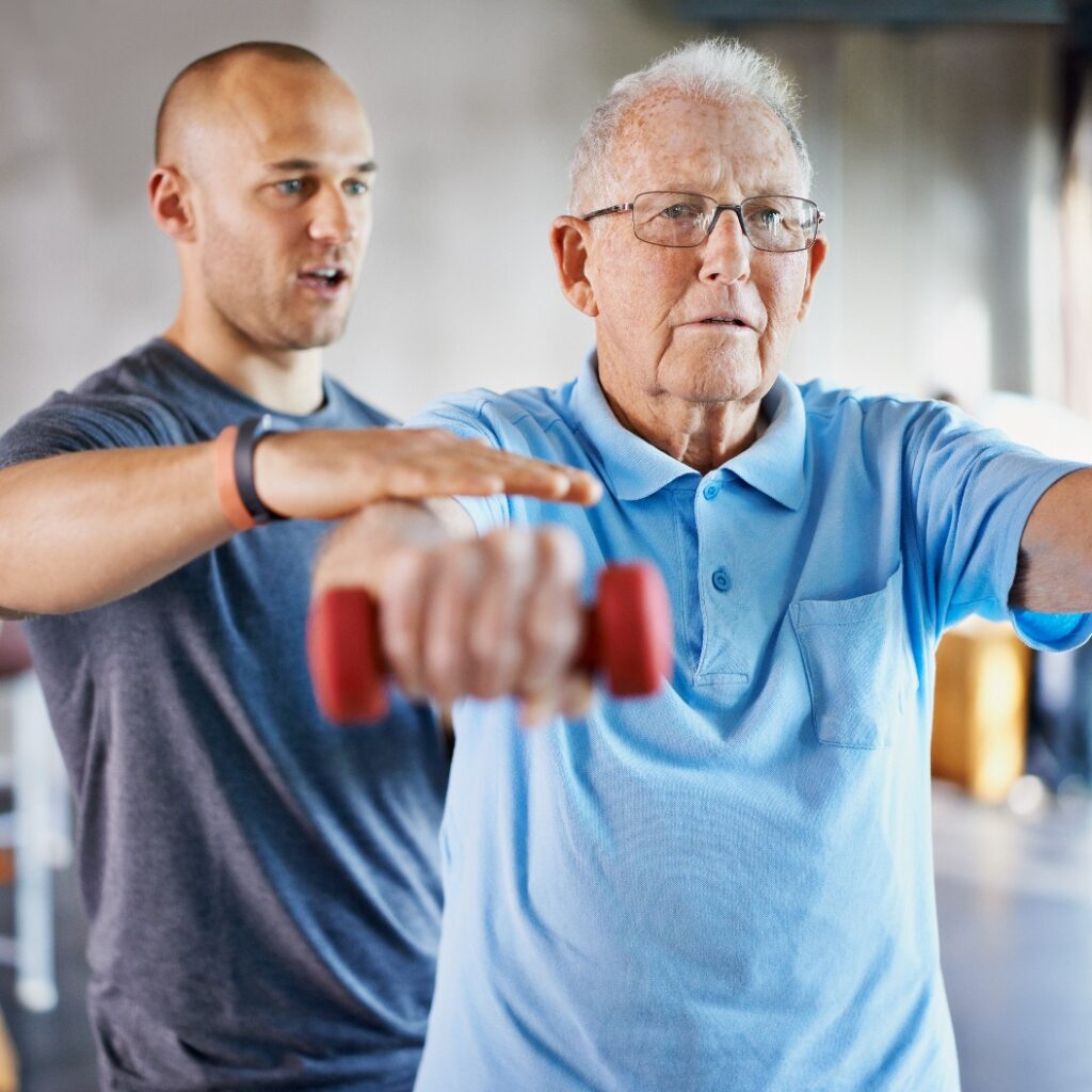 Rehabilitation ist nie einfach. Aufnahme eines Physiotherapeuten, der einem älteren Herrn beim Training mit Gewichten hilft.